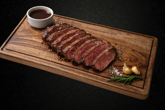 Valley of Craftsmen handmade wooden steak board with juice groove, featuring sliced steak, sauce, and herbs.